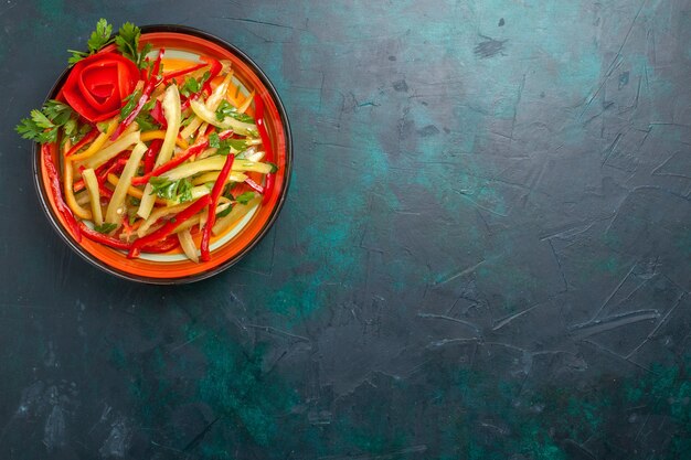 Top view sliced bell peppers different colored vegetable salad inside plate on the dark-blue background