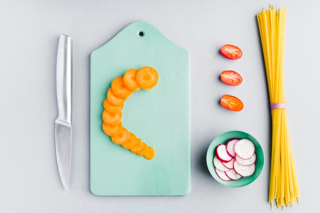 Top view sliced carrot on cutting board with uncooked spaghetti