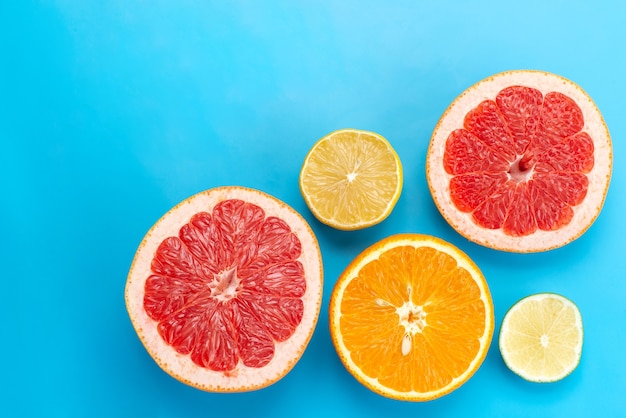 A top view sliced citruses grapefruits oranges and lemons on blue desk, citrus fruit juice