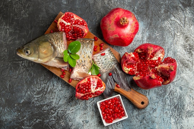 Top view sliced fresh fish with pomegranates on light-dark surface