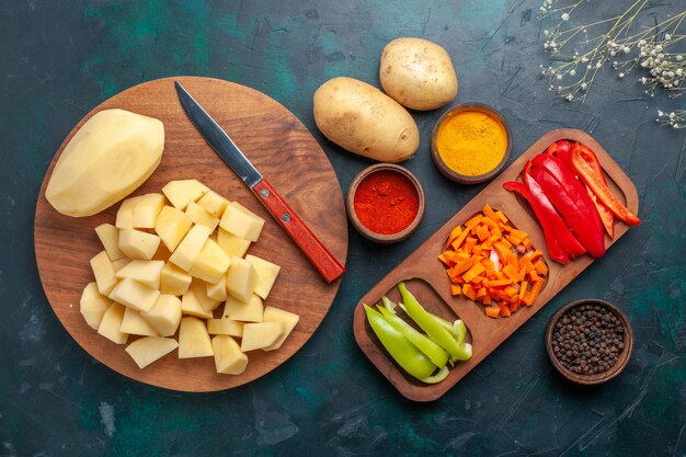 Top view sliced fresh potatoes with seasonings and sliced peppers on dark-blue desk