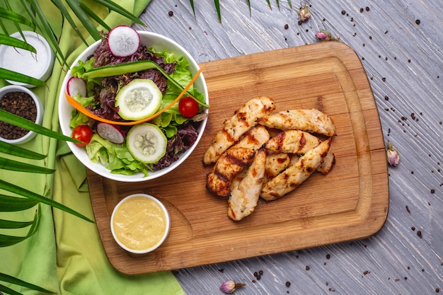 Top view sliced grilled chicken breast with vegetable salad and sauce on the board