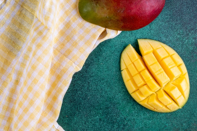 Free photo top view sliced mango with a yellow kitchen towel on green