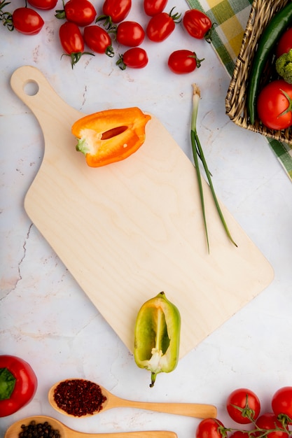 Top view of sliced peppers with scallion and other vegetables and cutting board on white surface