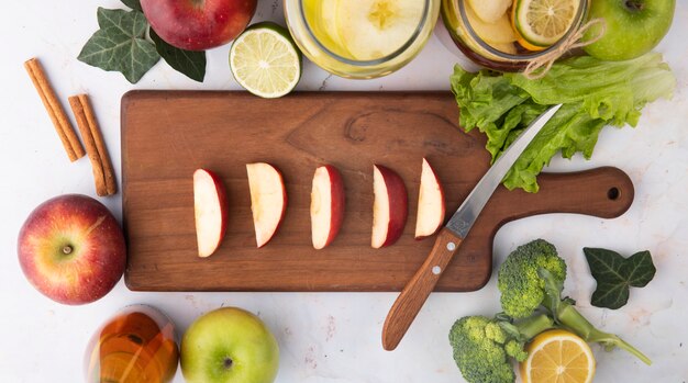 Top view sliced red apple on a board with lemon tea fresh apple juice brocoli cinnamon slice of lime and lettuce leaf