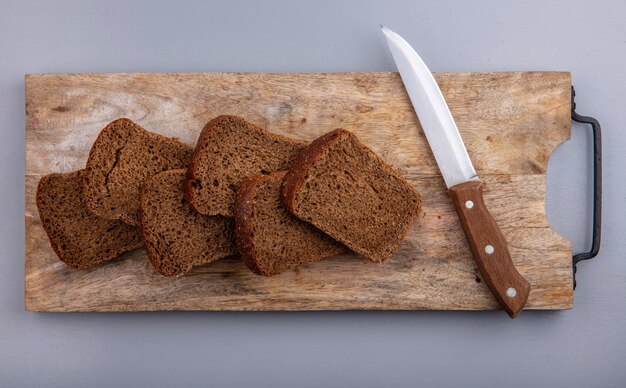 Top view of sliced rye bread and knife on cutting board on gray background