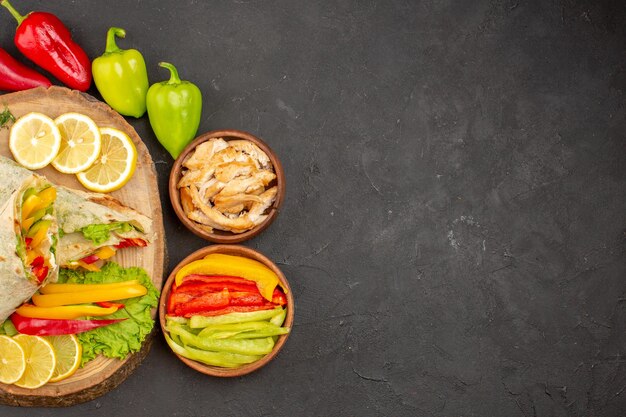 Top view of sliced shaurma meat sandwich with lemon slices and vegetables on black