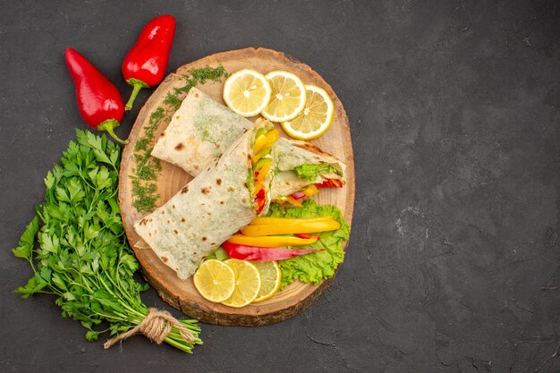 Top view of sliced shaurma meat sandwich with lemonnd greens on black