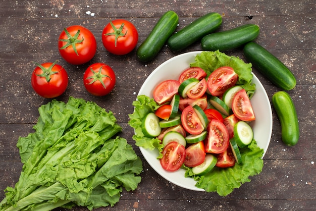 Top view sliced tomatoes with cucumbers inside white plate with green salad on brown, food vegetable fresh salad