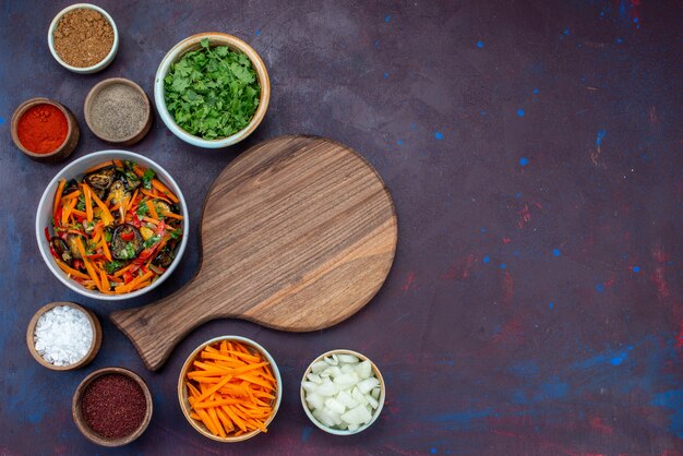 Top view sliced vegetable salad inside plate with greens seasonings on dark desk