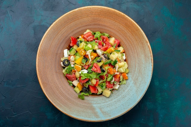 Top view sliced vegetable salad peppered inside plate on the dark-blue desk