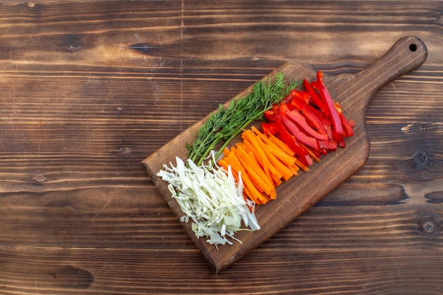 Top view sliced vegetables cabbage carrot greens and pepper on cutting board brown surface