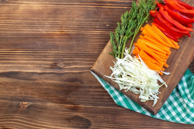 Top view sliced vegetables cabbage carrot greens and pepper on cutting board brown surface