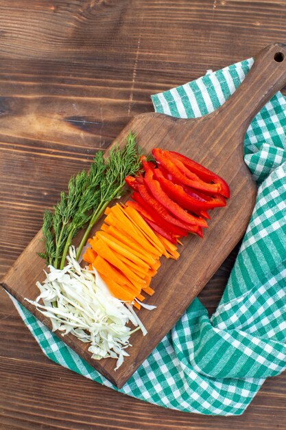 Top view sliced vegetables cabbage carrot greens and pepper on cutting board brown surface