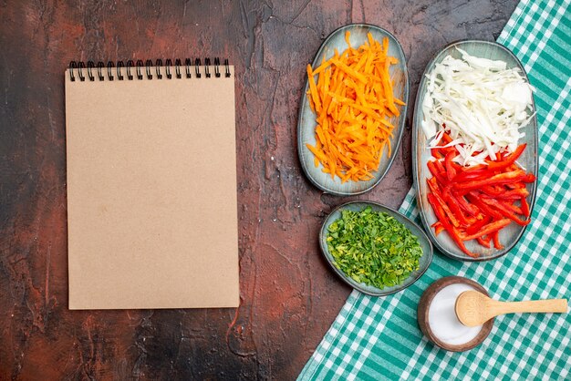 Top view sliced vegetables carrot cabbage and bell-pepper with greens on dark table