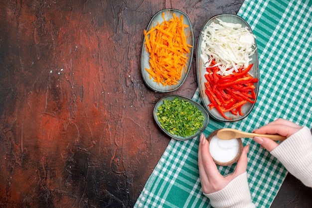 Top view sliced vegetables carrot cabbage and bell-pepper with greens on dark table