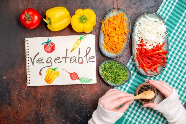 Top view sliced vegetables carrot cabbage and bell-pepper with greens on dark table