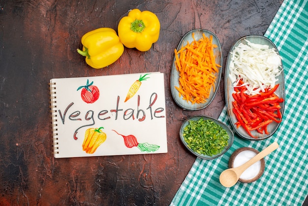 Top view sliced vegetables carrot cabbage and bell-pepper with greens on dark table