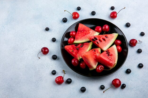 Top view slices of watermelon on a plate with blueberries and cherries