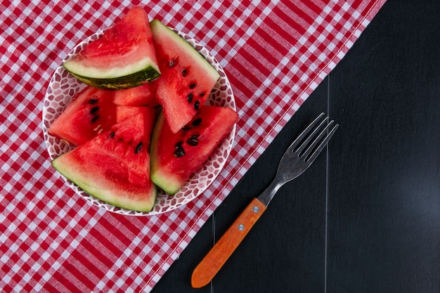 Free photo top view slices of watermelon on a red kitchen towel with a fork on a black background