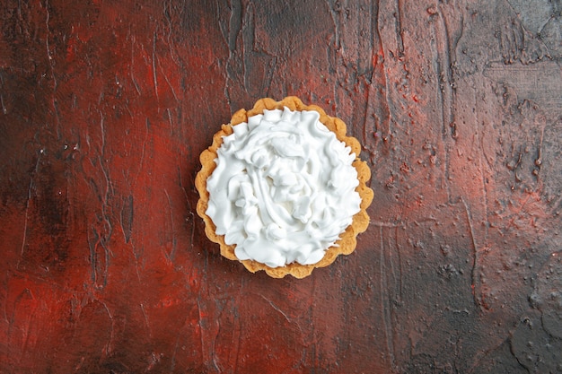 Top view of small tart with pastry cream on dark red surface