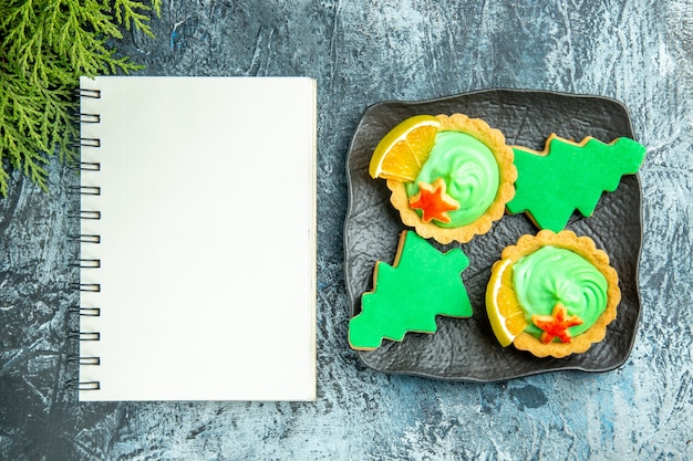 Free photo top view small tarts xmas tree biscuits on black plate notepad on grey table