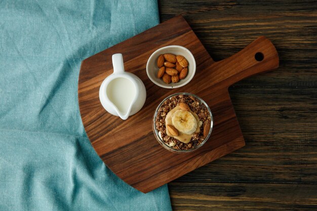 Top view of smoothie with banana almond walnut milk peanut butter in glass and milk with almond on cutting board on blue cloth on wooden background