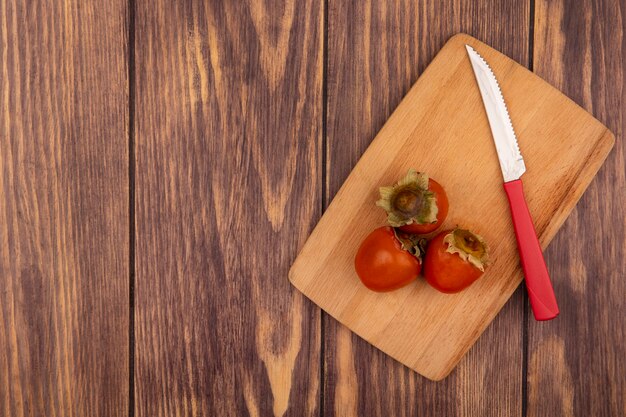 Top view of soft persimmons on a wooden kitchen board with knife on a wooden background with copy space