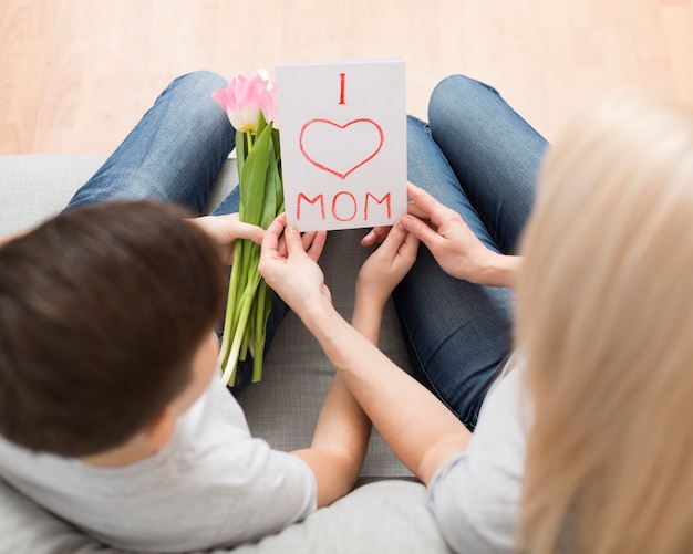 Top view son surprising mother with flowers and card