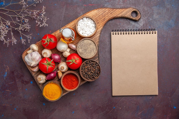 Free photo top view spices on the board spices tomatoes onions mushrooms and a bottle of oil on the cutting board and a notebook