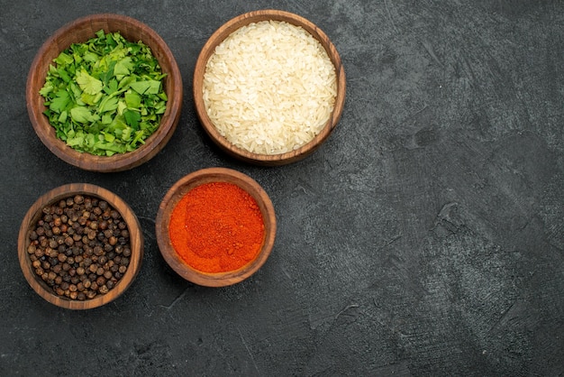 Top view spices in bowls black papper herbs colorful spices and rice on the left side of dark table