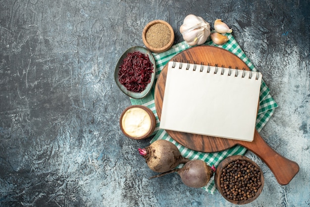 Free photo top view spiral notepad on wood board spices in bowls garlic beets on grey table with free space