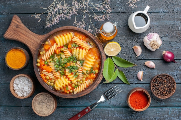 Top view spiral pasta soup with seasonings on dark-blue desk soup sauce color italian pasta cuisine dish