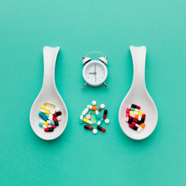 Free photo top view spoons with pills and clock