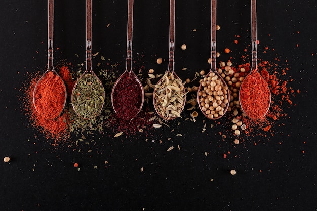 top view spoons with various pepper spices on black surface