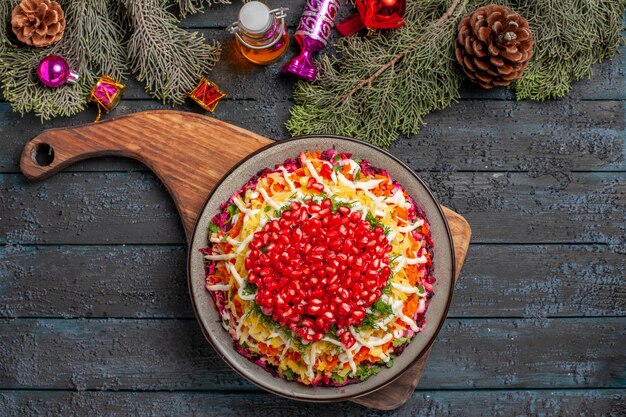 Top view spruce branches dish with seeds of pomegranate on the cutting board next to the spruce branches with cones and tree toys