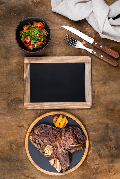 Free photo top view of steak on plate with salad and blackboard