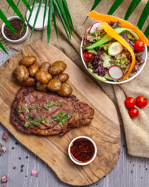 Free photo top view steak with potatoes and sauce on the board with salad and vegetables