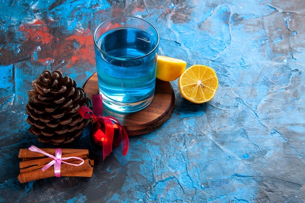 Free photo top view of a still water in a glass on wooden cutting board and lemons cinnamon limes conifer cone on the right side on blue background