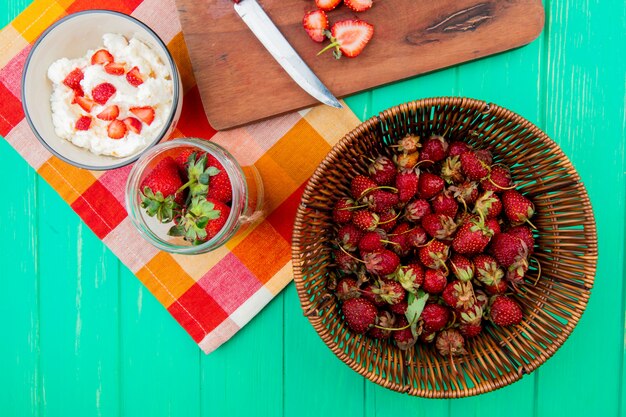 Top view of strawberries in basket with bowls of cottage cheese and strawberries on cloth on green surface