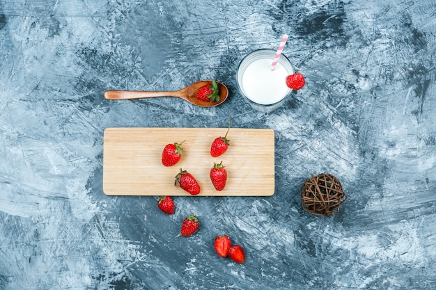 Top view strawberries on cutting board with milk,clew and a wooden spoon on dark blue marble surface. horizontal