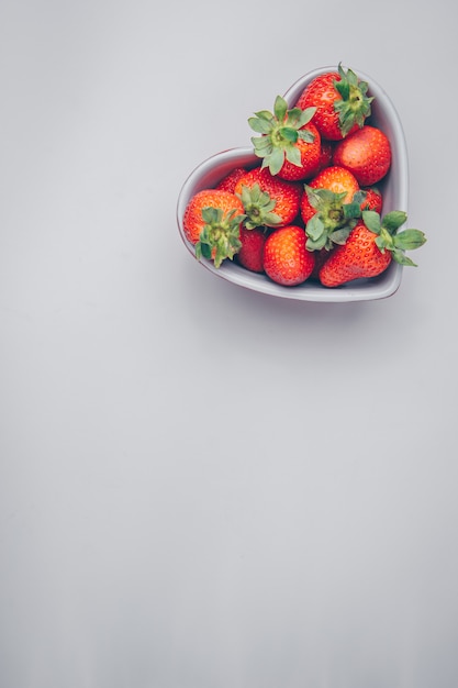 Free photo top view strawberries in heart shaped bowl on white background. vertical free space for your text