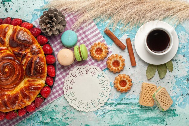 Top view strawberry pie with cookies french macarons and cup of tea on blue desk