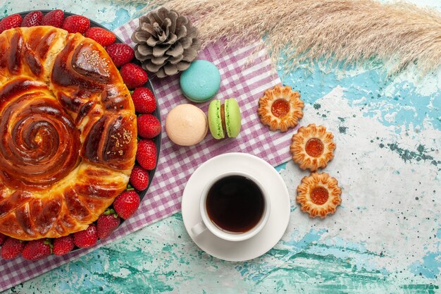 Top view strawberry pie with cookies macarons and cup of tea on blue surface