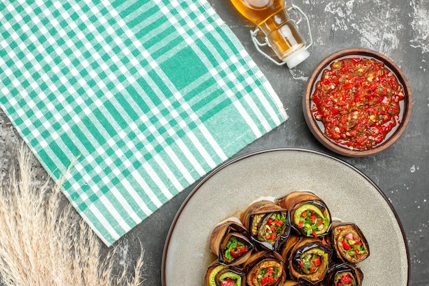 Free photo top view stuffed aubergine rolls in white oval plate adjika in small bowl turquoise-white tablecloth oil on grey surface