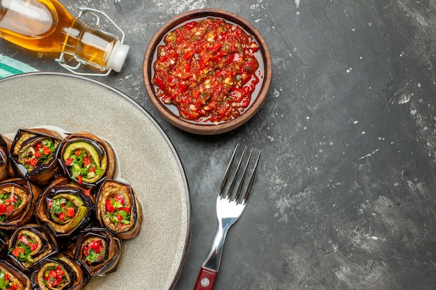 Free photo top view stuffed aubergine rolls in white oval plate fork oil adjika on grey background