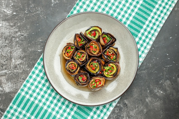 Top view stuffed aubergine rolls in white oval plate turquoise-white tablecloth on grey surface