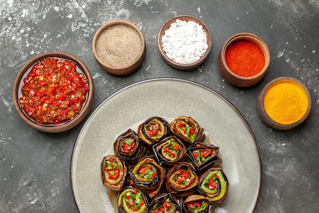 Top view stuffed eggplant rolls spices in small bowls salt pepper red pepper turmeric adjika on grey background