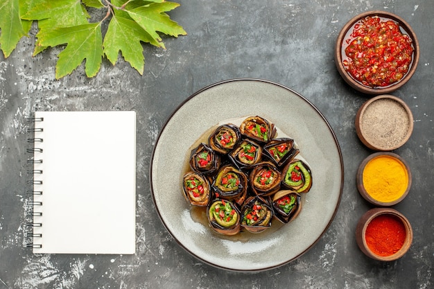 Free Photo top view stuffed eggplant rolls in white plate different spices adjika in small bowls a notebook on grey background