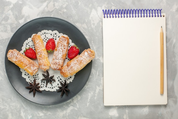 Free photo top view of sugar powdered bagels delicious dough with strawberries and notepad on white surface